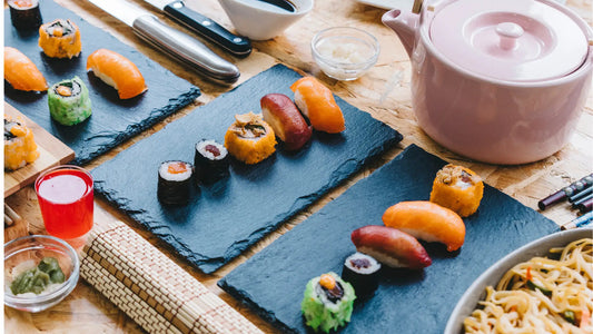 Assortiment de sushi japonais avec maki et nigiri colorés, accompagné d’une théière et de baguettes, illustrant la richesse de la gastronomie japonaise.