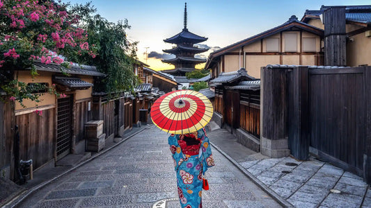 Femme en kimono avec un parapluie traditionnel marchant dans une rue de Kyoto, avec une pagode en arrière-plan au coucher du soleil.