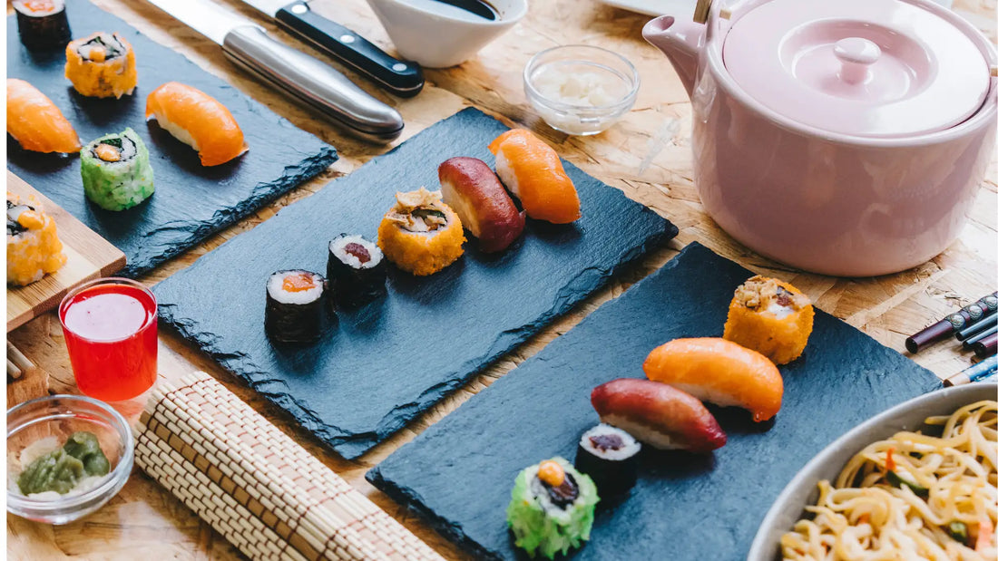 Assortiment de sushi japonais avec maki et nigiri colorés, accompagné d’une théière et de baguettes, illustrant la richesse de la gastronomie japonaise.